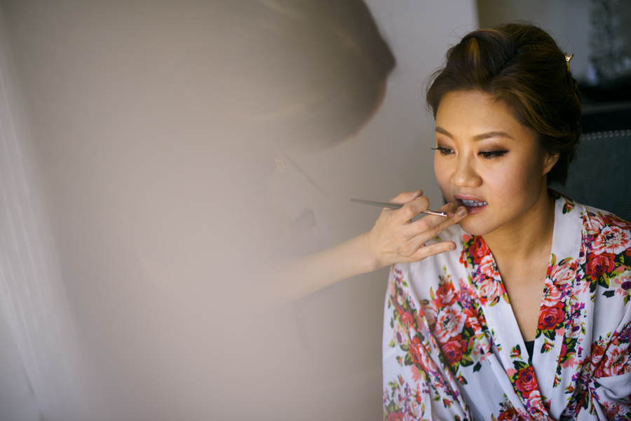 A cool image of a bride getting her make up retouched before getting into her dress